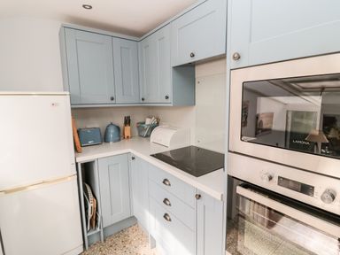 A kitchen with light blue cabinets a white refrigerator stainless steel oven toaster kettle and knife block at Lyndhurst Cottage in Beadnell