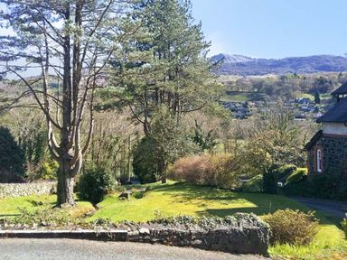 A garden with trees bushes and stone wall overlooking hills and a village at Llechwedd in Dolgellau