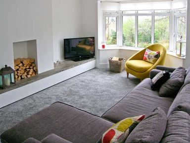 A living room with a grey sofa and a yellow armchair near a bay window with a television and a fireplace with firewood at Llechwedd in Dolgellau