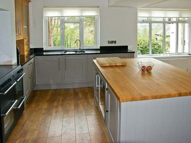 A kitchen with wooden flooring a central island with a wooden countertop and cabinets under windows at Llechwedd in Dolgellau
