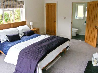 A bedroom with a bed a nightstand a lamp two wooden doors and an en suite bathroom at Llechwedd in Dolgellau