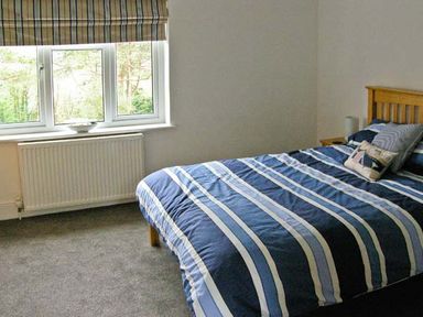 A bedroom with a bed covered in striped bedding next to a window and radiator at Llechwedd in Dolgellau