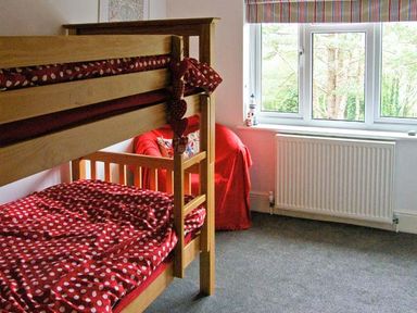 A bedroom with wooden bunk beds with red polka dot bedding a red armchair and a window at Llechwedd in Dolgellau