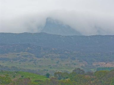 A misty mountain peak with rolling hills and scattered trees in the foreground at Llechwedd in Dolgellau