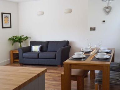 A living room with a dark grey sofa a wooden dining table set with white bowls and glasses and a wooden side table with a plant at Llechwedd in Dolgellau