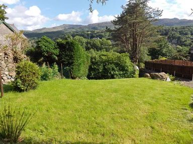 A grassy garden with bushes trees and a wooden fence with hills in the background at Llechwedd in Dolgellau