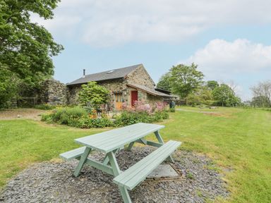 A picnic table on a gravel area in a garden with a stone cottage and flowers at The Shippon in Llechwedd The Conwy Valley