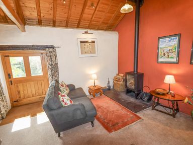 A living room with a wooden ceiling a gray sofa a wood stove and wooden tables at The Shippon in Llechwedd The Conwy Valley