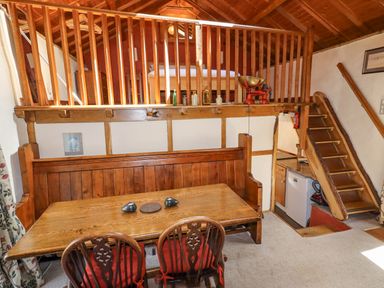 A dining area with a wooden table and chairs below a loft bed accessed by wooden stairs at The Shippon in Llechwedd The Conwy Valley