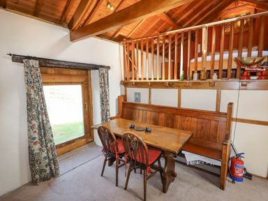 A dining area with a wooden table two chairs a bench and a loft above at The Shippon in Llechwedd The Conwy Valley