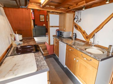 A kitchen with wooden cabinets a stove and sink leading to a living room at The Shippon in Llechwedd The Conwy Valley