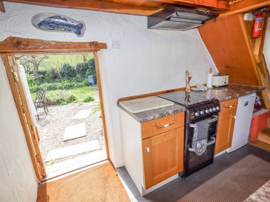 A small kitchen with wooden cabinets a stove a cutting board and an open door leading to a garden at The Shippon in Llechwedd The Conwy Valley