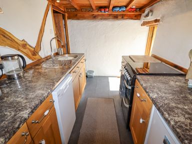 A kitchen with wooden cabinets a stove a sink and a countertop at The Shippon in Llechwedd The Conwy Valley