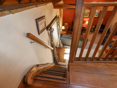 A view down wooden stairs to a living room with sofas lamps and framed pictures at The Shippon in Llechwedd The Conwy Valley