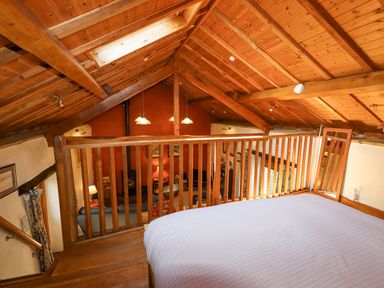 A loft bedroom with a bed and wooden railing overlooking a living area with furniture at The Shippon in Llechwedd The Conwy Valley