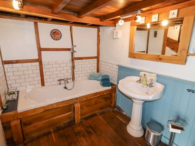 A bathroom with a wooden framed bathtub and pedestal sink with mirror at The Shippon in Llechwedd The Conwy Valley