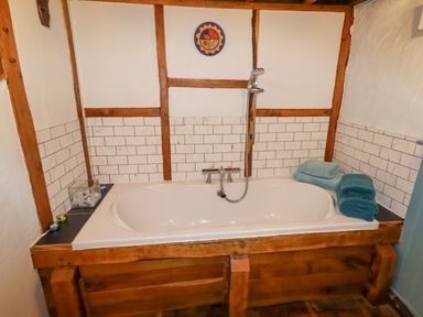 A bathroom with a white bathtub surrounded by wooden paneling and white tiled walls with towels on the edge at The Shippon in Llechwedd The Conwy Valley
