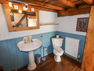 A bathroom with a pedestal sink a toilet a mirror a radiator and wooden beams at The Shippon in Llechwedd The Conwy Valley