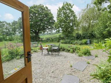 A garden patio with a small round table and two chairs surrounded by plants and trees at The Shippon in Llechwedd The Conwy Valley