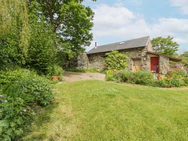 A stone house with a garden and green lawn surrounded by trees and flowers at The Shippon in Llechwedd The Conwy Valley