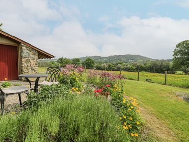 A garden with flowers and a small round table with two chairs outside a stone building in a rural area at The Shippon in Llechwedd The Conwy Valley