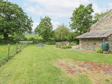 A garden with a picnic table flowers and a stone building at The Shippon in Llechwedd The Conwy Valley