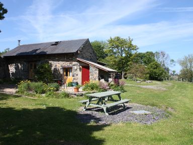 A stone cottage with wooden doors and a picnic table on grass surrounded by trees and flowers at The Shippon in Llechwedd The Conwy Valley