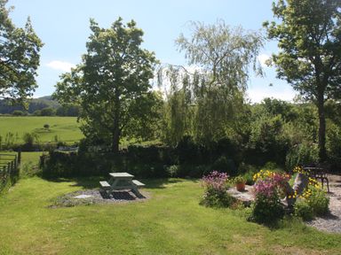 A garden area with a picnic table on grass and flowers around a stone feature at The Shippon in Llechwedd The Conwy Valley