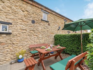 An outdoor patio with wooden benches and table set with plates and drinks next to a stone wall and green umbrella at Upstairs Downstairs Cottage in Snainton near Scarborough