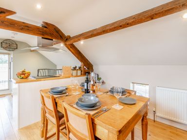 A dining table set with plates glasses and cutlery under wooden beams in an open kitchen at Upstairs Downstairs Cottage in Snainton near Scarborough