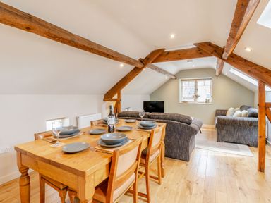 A dining area with a wooden table and chairs set with plates and glasses next to a sitting area with two sofas and a television at Upstairs Downstairs Cottage in Snainton near Scarborough