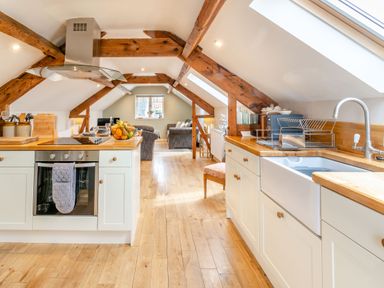 A kitchen with wooden beams and countertops with an oven and sink next to a seating area at Upstairs Downstairs Cottage in Snainton near Scarborough