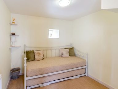 A small bedroom with a daybed and cushions next to corner shelves with a lamp and a basket on the floor at Upstairs Downstairs Cottage in Snainton near Scarborough