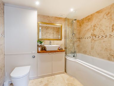 A bathroom with a toilet, sink with a wooden counter, mirror, and bathtub with a shower at Upstairs Downstairs Cottage in Snainton near Scarborough