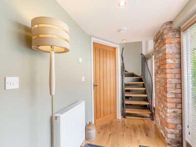 A hallway with a floor lamp radiator wooden door staircase and exposed brick wall at Upstairs Downstairs Cottage in Snainton near Scarborough