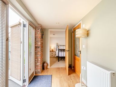 A hallway with wooden floor and open door leading to a bedroom with a metal bed at Upstairs Downstairs Cottage in Snainton near Scarborough