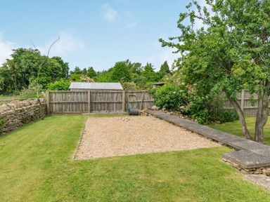 A gravel area with metal balls and a concrete bench surrounded by grass and trees at Upstairs Downstairs Cottage in Snainton near Scarborough
