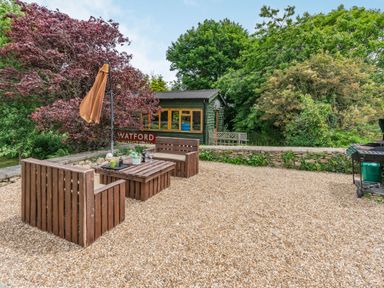 An outdoor seating area with wooden benches and table on gravel near a green shed and trees at Upstairs Downstairs Cottage in Snainton near Scarborough