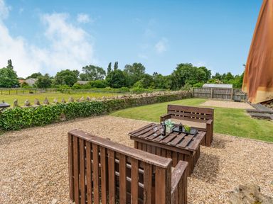 A garden with wooden furniture on gravel and a fenced grassy area at Upstairs Downstairs Cottage in Snainton near Scarborough