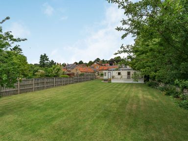 A large grassy garden with trees, a wooden fence, and a small white building at Upstairs Downstairs Cottage in Snainton near Scarborough