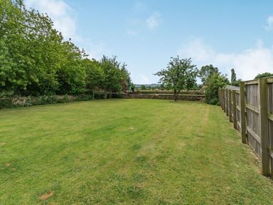A large grassy garden with trees along the back and a wooden fence on the right at Upstairs Downstairs Cottage in Snainton near Scarborough