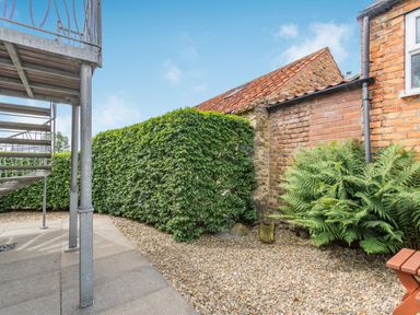 An outdoor area with metal spiral staircase gravel ground green hedge and brick walls at Upstairs Downstairs Cottage in Snainton near Scarborough