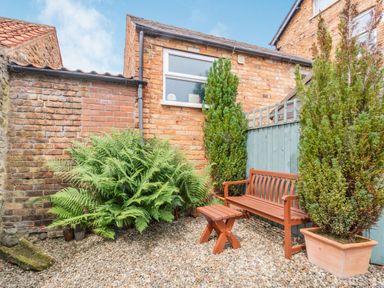 A small garden area with a wooden bench and stool surrounded by plants and brick walls at Upstairs Downstairs Cottage in Snainton near Scarborough