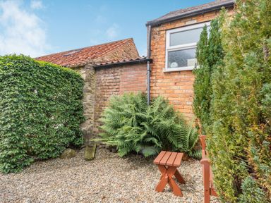 A small outdoor area with gravel ground a wooden stool and green plants at Upstairs Downstairs Cottage in Snainton near Scarborough