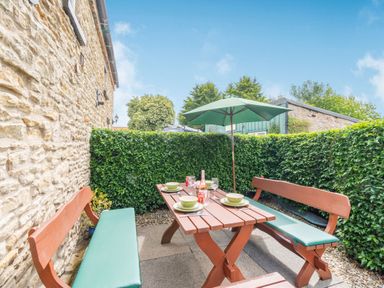 An outdoor patio area with a wooden table and benches under a green umbrella at Upstairs Downstairs Cottage in Snainton near Scarborough