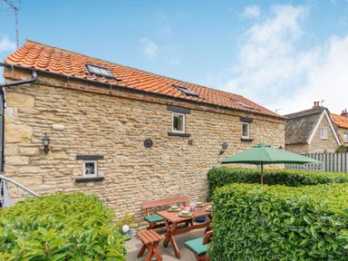 An outdoor patio area with wooden table and benches surrounded by hedges at Upstairs Downstairs Cottage in Snainton near Scarborough