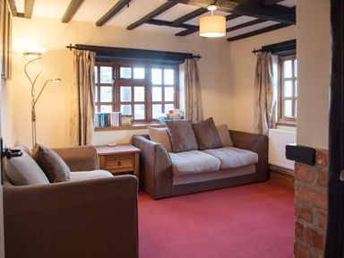 A living room with two sofas a wooden side table books on windowsill and curtains at Yew Tree Cottage in Little Malvern near Malvern