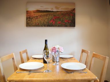 A dining table set with white plates wine glasses cutlery and a bottle of wine under a wall painting of a field at Yew Tree Cottage in Little Malvern near Malvern