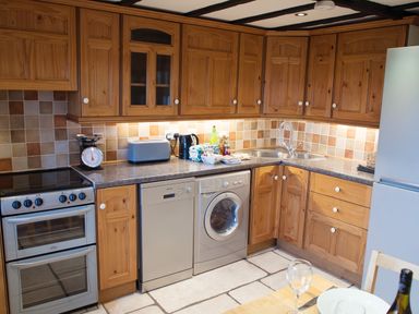 A kitchen with wooden cabinets a stove dishwasher washing machine and a sink at Yew Tree Cottage in Little Malvern near Malvern