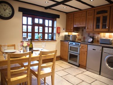 A kitchen with wooden cabinets dining table set with plates wine glass and bottle at Yew Tree Cottage in Little Malvern near Malvern